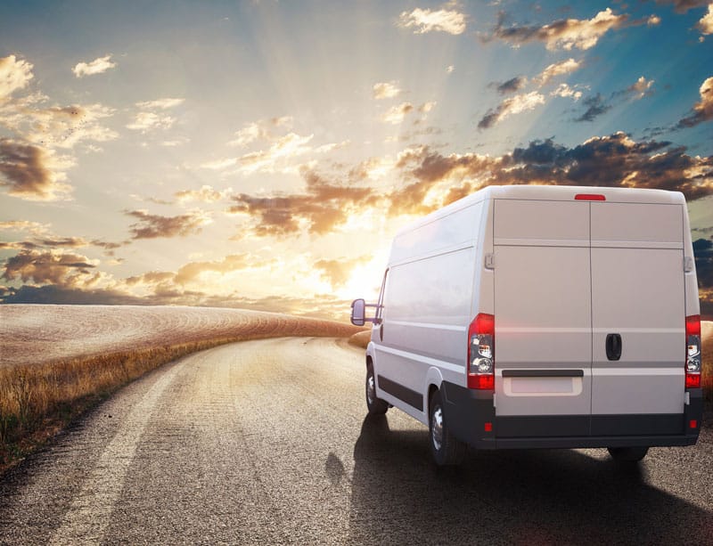 A van driving down the road with sun setting in the background.