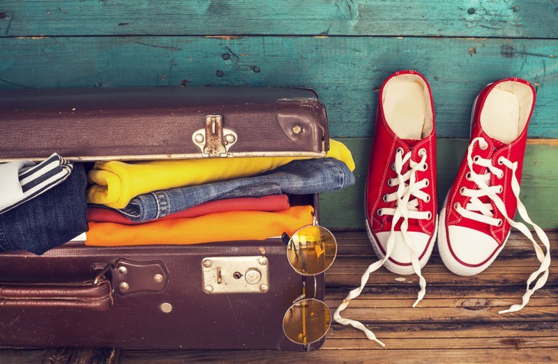 A pair of red tennis shoes and some clothes on top of a suitcase.