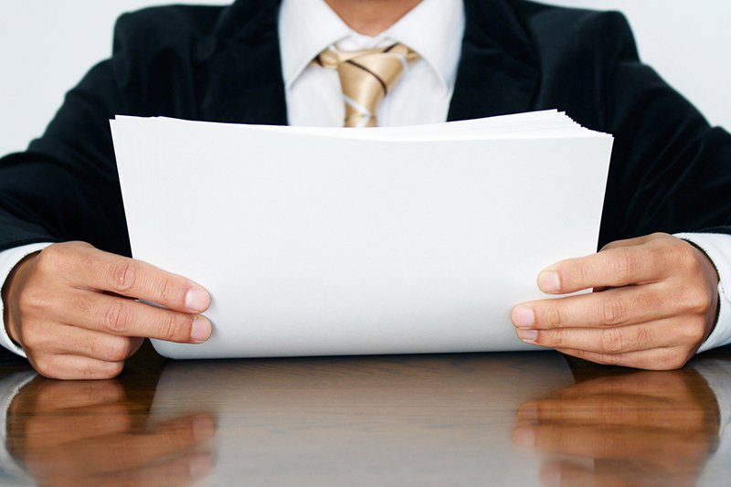 A man in black jacket holding papers on table.