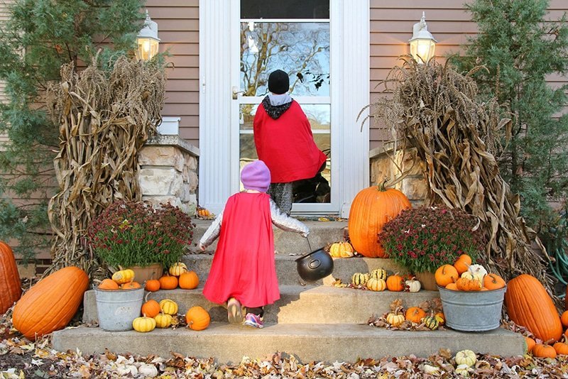 Two children in costumes are entering a house.