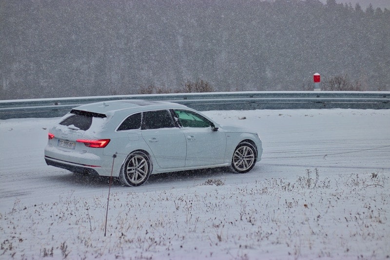 A white car driving on the road in snow.