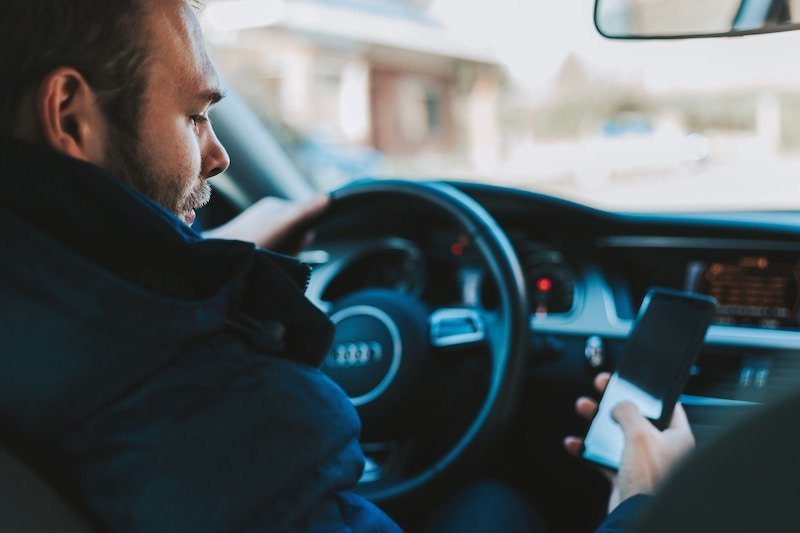 A man sitting in the driver 's seat of his car while looking at his phone.