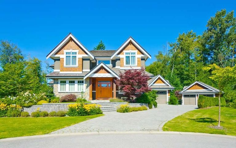 A large house with a driveway and flowers in front of it.