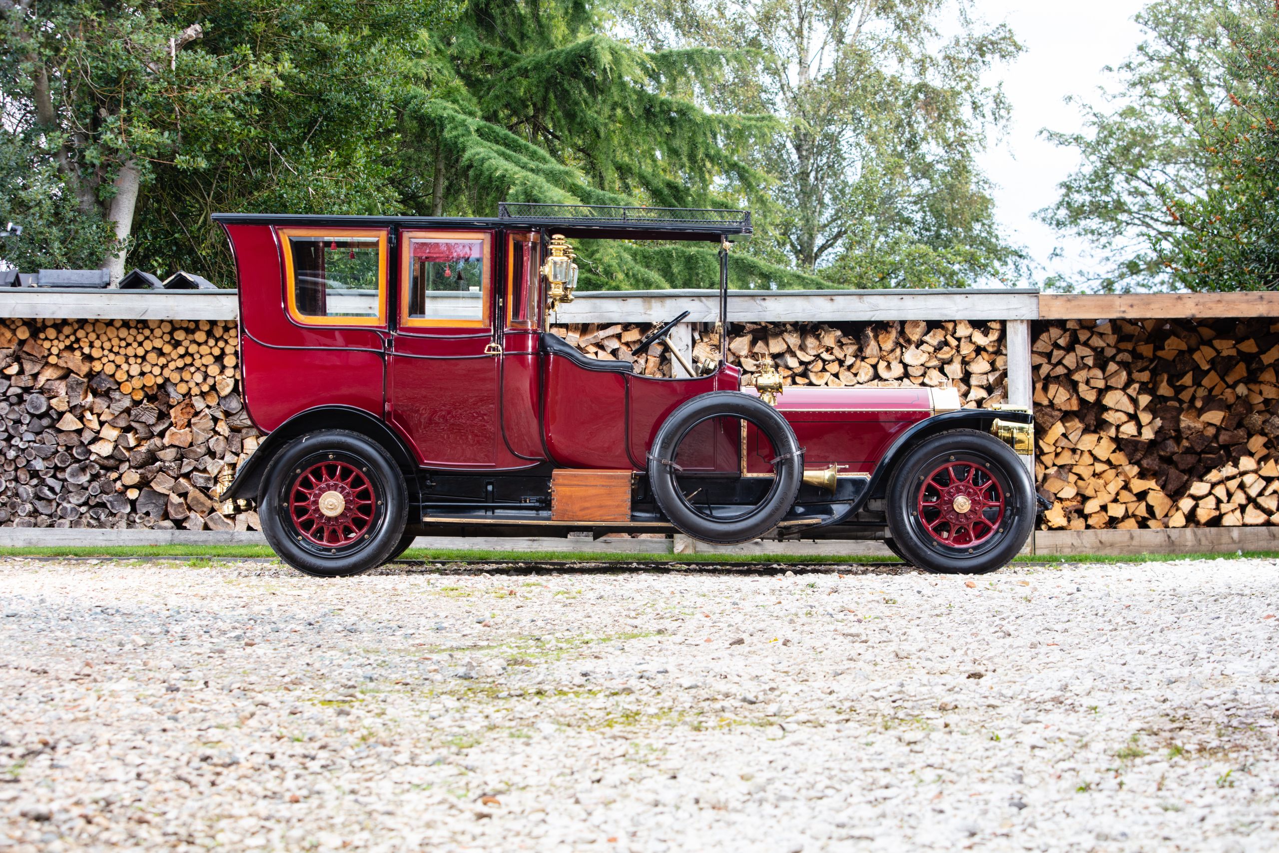 A red car parked in front of a pile of wood.