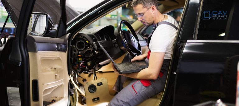 A man sitting in the drivers seat of a car with his laptop.